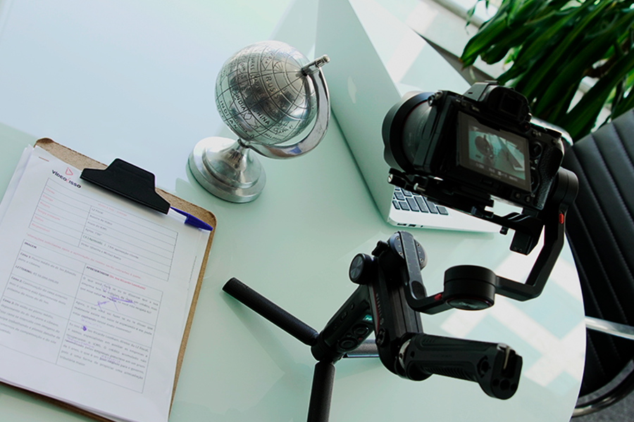 Roteiro de vídeo institucional sob a mesa, e ao lado, uma câmera de vídeo e um globo de prata.