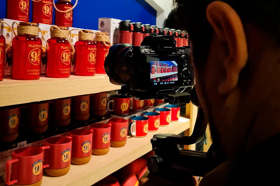 Homem com câmera de vídeo gravando produtos de Harry Potter, que são garrafas.